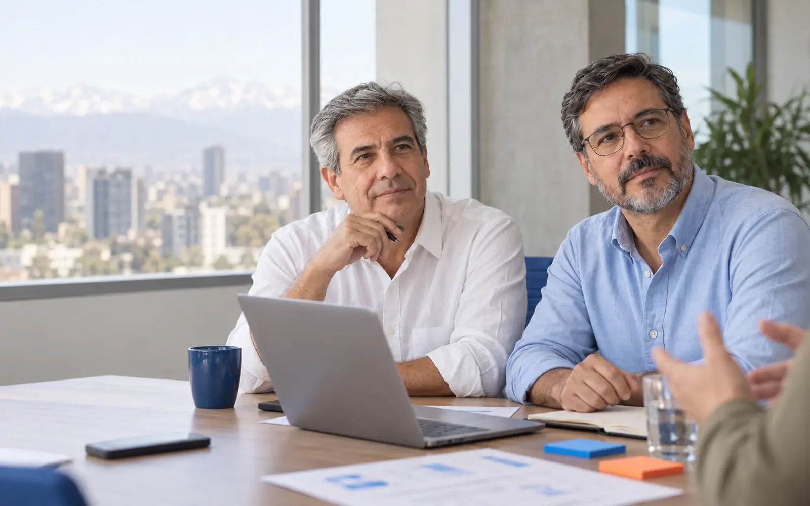 Dos personas escuchan durante una revisión con laptop y documentos.